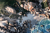 Luftaufnahme einer Bucht, abgelegener Strand, umgeben von hoch aufragenden Felsen und blauem Meerwasser, das auf den Strand rollt, Kapstadt, Westkap, Südafrika