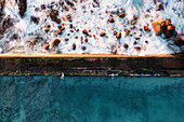 Aerial view of a tidal rock pool,taken with a long exposure shutter setting,showing the waves crashing onto the rocks and two people swimming in the pool,Cape Town,Western Cape,South Africa