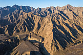 Luftaufnahme eines Canyons zwischen felsigen und trockenen Bergen in der Wüste im Staat Ajman, Vereinigte Arabische Emirate