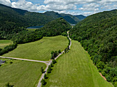 Luftaufnahme eines üppig grünen Tals, umgeben von majestätischen Bergen, mit einer kurvenreichen Straße und Feldern, Kruth, Frankreich