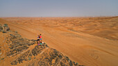 Aerial view of two girls waving on a rocky mountain in the Camel Rock Desert Safari in UAE