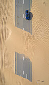 Luftaufnahme eines Autos, das auf einer mit Sand bedeckten Straße in der Wüste von Dubai, Vereinigte Arabische Emirate, fährt