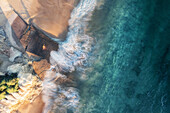 Aerial view of two people standing on a beach boat ramp at sunset,overlooking the clear blue water while the waves roll onto shore with a long exposure,Port Noarlunga,South Australia,Australia