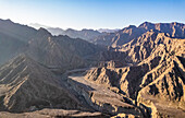 Luftaufnahme eines Canyons zwischen den felsigen und trockenen Bergen in der Wüste im Staat Ajman, Vereinigte Arabische Emirate