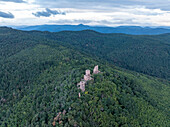 Luftaufnahme einer ruhigen Burgruine, umgeben von üppigem Wald und majestätischen Bergen, Husseren-les-Chateaux, Frankreich