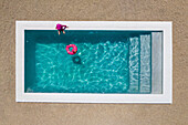 Aerial view of a girl wearing a pink costume sitting by a pool with clear blue water and a pink flamingo floatie in the pool,Cape Town,Western Cape,South Africa