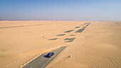 Luftaufnahme eines Autos, das auf einer mit Sand bedeckten Straße in der Wüste von Dubai, Vereinigte Arabische Emirate, fährt