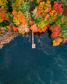 Aerial view of vibrant autumn foliage reflecting on serene North Pond with a dock and surrounding forest,Bryant Pond,Maine,United States