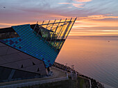 HULL,ENGLAND - 12 JAN 2022 : Luftaufnahme der Deep und der Humber-Mündung bei Sonnenaufgang während der Goldenen Stunde mit sanftem orangefarbenem Licht, das sich auf dem Wasser spiegelt und die Szene beleuchtet