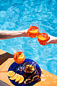 Two people drinking Aperol Spritz by the pool