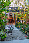 Kleiner Innenhofgarten mit Birken, Lounge-Stühlen und üppiger Bepflanzung