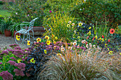 Blumenbeet mit Dahlien (Dahlia), Fetthennen (Sedum) und Ziergräsern neben Kiesweg und Metallbank