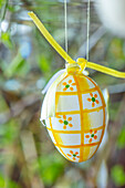 Osterei mit gelben Karos und Blumenmuster an gelbem Band aufgehängt