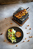 Satay skewers on a table grill with peanut sauce and salad