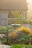 Romantischer Landgarten mit Wasserbrunnen und Gartenhaus im Frühling
