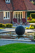 Moderner Garten mit Wasserskulptur und Liegestühlen vor Backsteinfassade