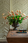 Tulpen (Tulipa) in Metallgefäß auf Holztisch vor verzierter Wand