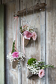 Hängende Blumenkörbchen mit Nelken (Dianthus) und Schleierkraut an Holzwand