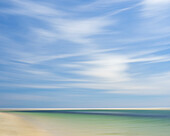 Blur of beach, clouds, and sky.