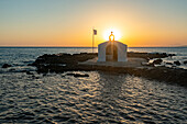 Romantischer Himmel bei Sonnenaufgang über der kleinen griechischen Kirche auf einem Inselchen im rauen Meer, Georgioupolis, Insel Kreta, Griechenland
