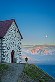 Back view of a hiker admiring Dolomites from Latzfonser Kreuz at sunset with full moon, Lazfons, Chiusa, Bolzano district, South Tyrol, Italy, Europe.