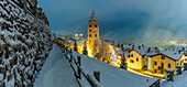 Church of Saint Pantalon and snow covered town centre and mountainous background in winter at dusk, Courmayeur, Aosta Valley, Italian Alps, Italy