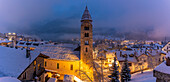 Church of Saint Pantalon and snow covered town centre and mountainous background in winter at dusk, Courmayeur, Aosta Valley, Italian Alps, Italy