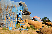 Painter working on Painted Rocks site, work of the Belgian artist Jean Verame, around Tafraout, Anti-Atlas, Morocco