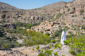 Mann in Dishdasha bewundert altes Lehmdorf in den Ruinen von Al Ain, hochgelegene Dörfer des Jabal Al Akhdar (Grüne Berge) um das Sayq-Plateau, Oman