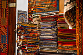 Stacks of vibrant handwoven Moroccan rugs and carpets displayed in a traditional shop in Fes, Morocco