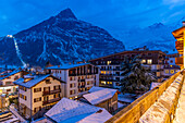 View of snow covered rooftops with mountainous background at dusk, Courmayeur, Aosta Valley, Italy