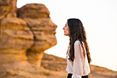 Woman in front of Face Rock, a sandstone rock formation in shape of human head profile, Hegra, UNESCO, AlUla, Medina Province, Saudi Arabia