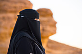 Woman in a niqab at Face Rock, a sandstone rock formation in shape of human head profile, Hegra, UNESCO, AlUla, Medina Province, Saudi Arabia