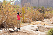 Woman photographing Palm plantation colonized by invasive Sodom apple (Calotropis procera), Sharaan Nature Reserve, Medina Province, Saudi Arabia