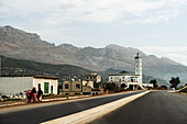 Rural road through a Moroccan village with a mosque and towering mountains in the distance, Morocco