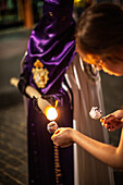 A Nazareno pours molten wax for a young girl, creating a festive ball during Holy Week celebrations in Seville, Andalusia, Spain.