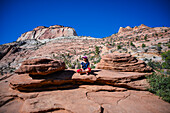 Junge kaukasische Frau sitzt mit gekreuzten Beinen auf dem Canyon Overlook Trail im Zion National Park, Utah