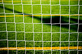 An artistic close-up of a football goal net in a green sports field.