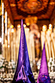 During Holy Week in Seville, penitents stand before the Virgin of Victory’s canopy, surrounded by glowing devotional candles.