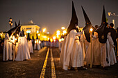 Nazarenos from the Estrella brotherhood walk with candles in the night of Palm Sunday, celebrating Holy Week in Seville.