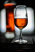 Ein mit Palo-Cortado-Sherrywein gefülltes Glas steht elegant vor einer Flasche, die den satten Bernsteinton vor einem verschwommenen Hintergrund zur Geltung bringt.