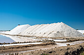 Large salt mounds rise against a clear blue sky in the salt flats of Sanlucar de Barrameda, located in Andalusia, Spain.