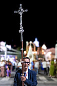 A devoted parishioner leads the procession in Castilleja del Campo by holding a crucifix, showcasing faith during the celebration.