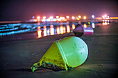 Yellow buoy on sandy beach at night reflecting bright lights in Cadiz, Spain