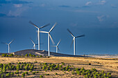 Tall wind turbines stand against a dramatic sky in Provincia de Soria, showcasing renewable energy amidst a stunning natural backdrop.