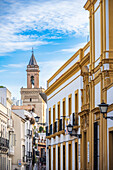 Charming view of La torre de la iglesia de San Marcos framed by historic buildings on San Luis Street in beautiful Seville, Spain.
