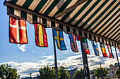 Flags from various countries hang from the awning of a bar in Oslo, showcasing international diversity on a sunny day.