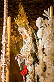 Virgen Macarena showcases her beauty in profile, surrounded by varales and wax flowers during Holy Week in Seville, Andalusia.