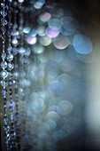 Intricate beaded glass curtain displays delicate patterns in soft focus, highlighting a captivating ambiance and shimmering bokeh.