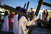 A procession of cloaked penitents carrying large wooden crosses during Holy Week in Spain.